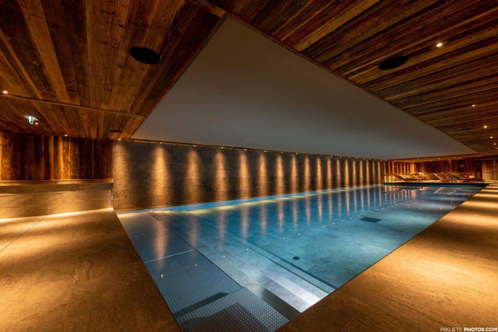 Elegantes Hallenbad mit sanfter Beleuchtung und modernem Holzdesign, ideal für Entspannung nach sportlichen Abenteuern.