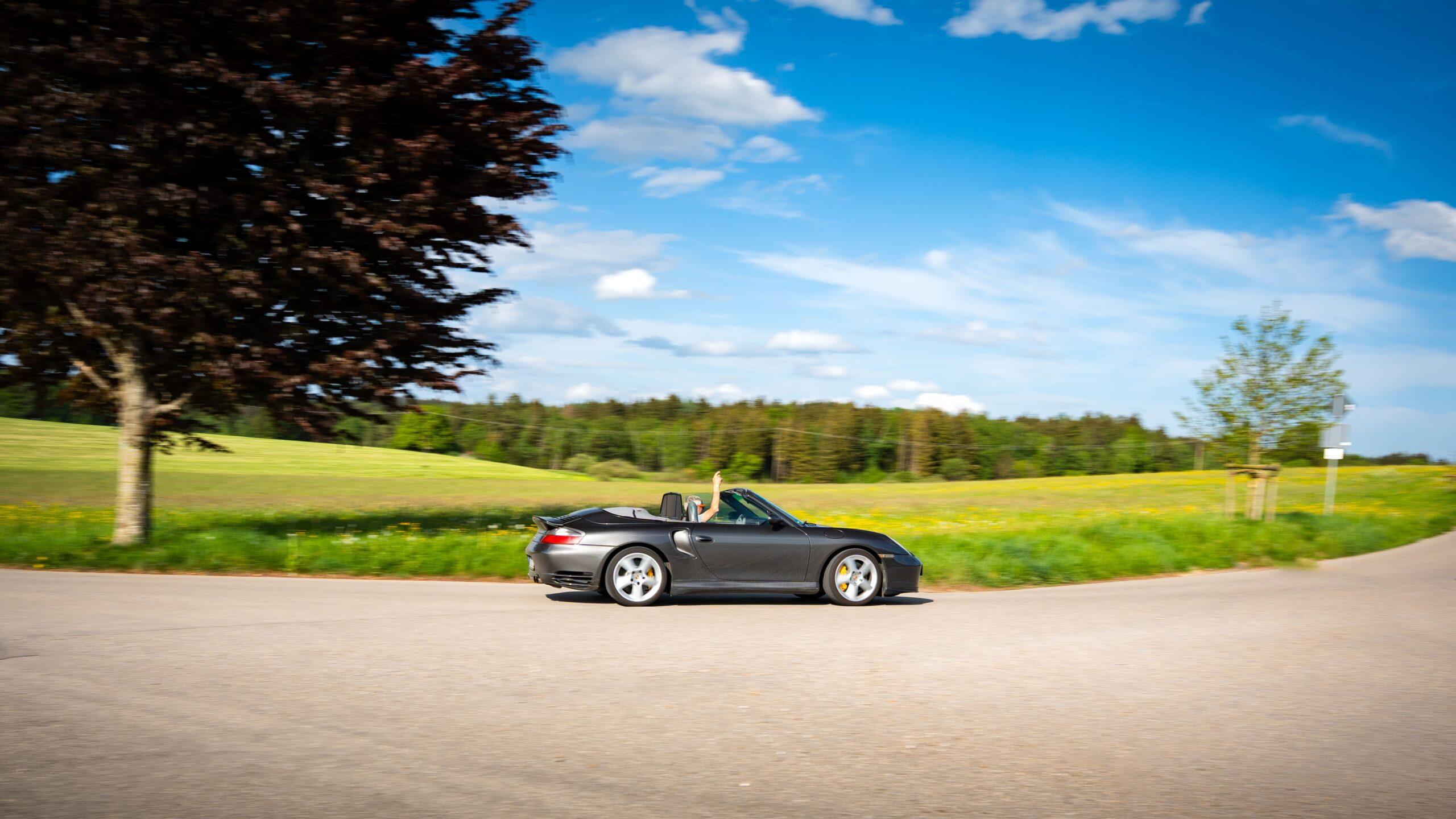Ein Sportwagen fährt auf malerischer Landstraße im Grünen bei sonnigem Wetter.
