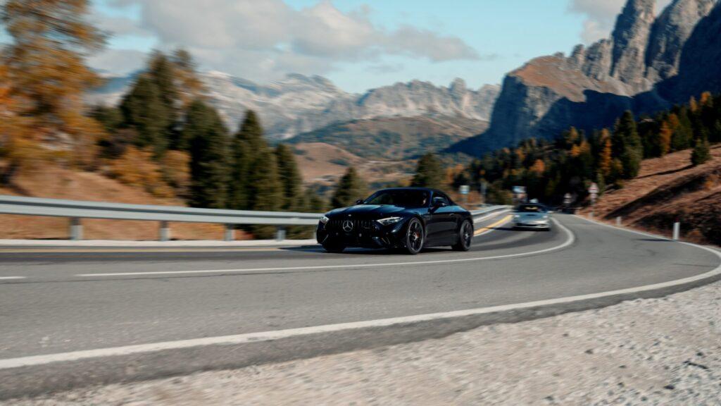 Schwarzes Sportauto kurvenreich in den atemberaubenden Dolomiten, umgeben von leuchtenden herbstlichen Farben.
