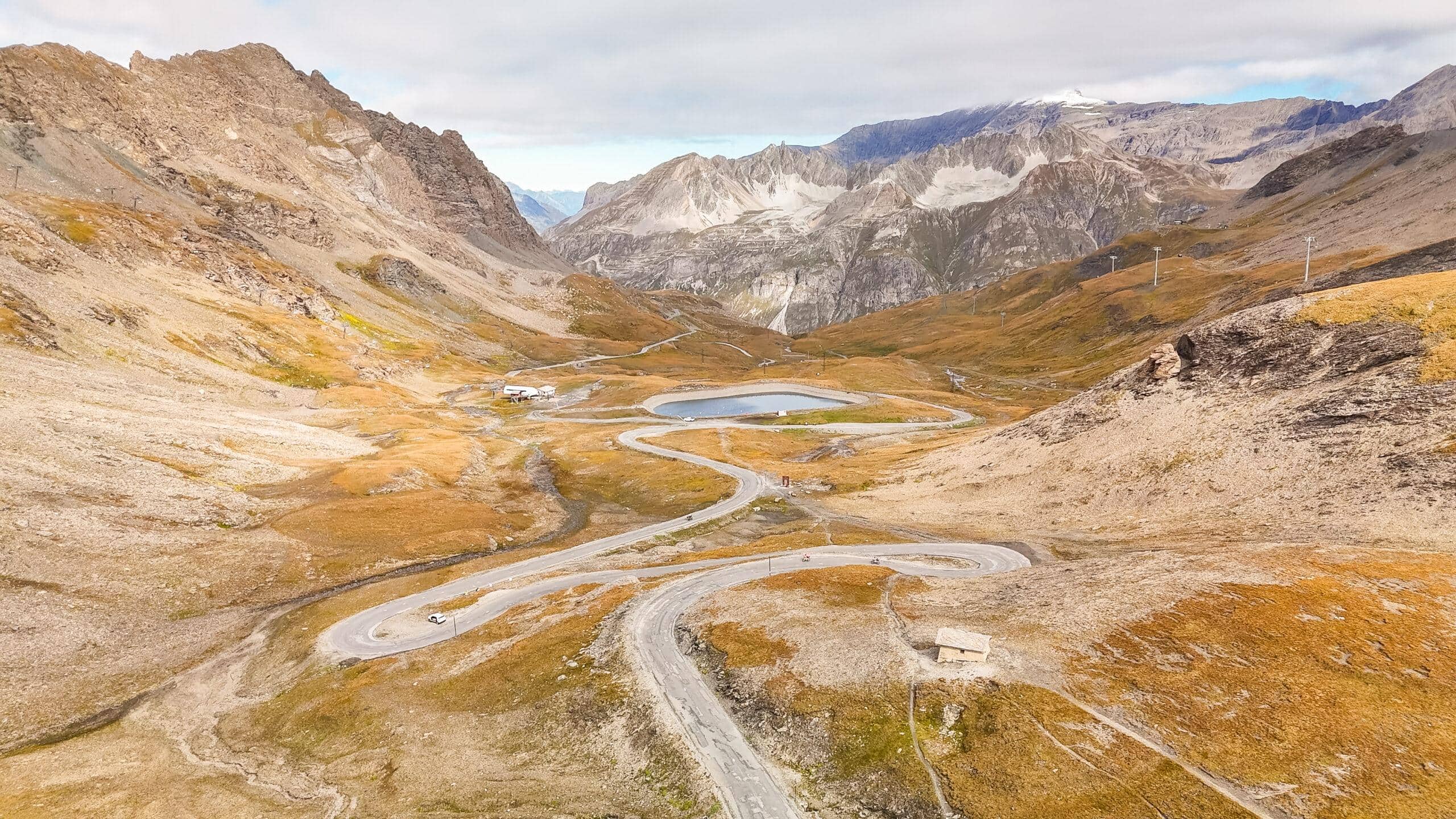 Kurvenreiche Alpenstraße zwischen majestätischen Bergen, umgeben von herbstlicher Landschaft und einem Bergsee.