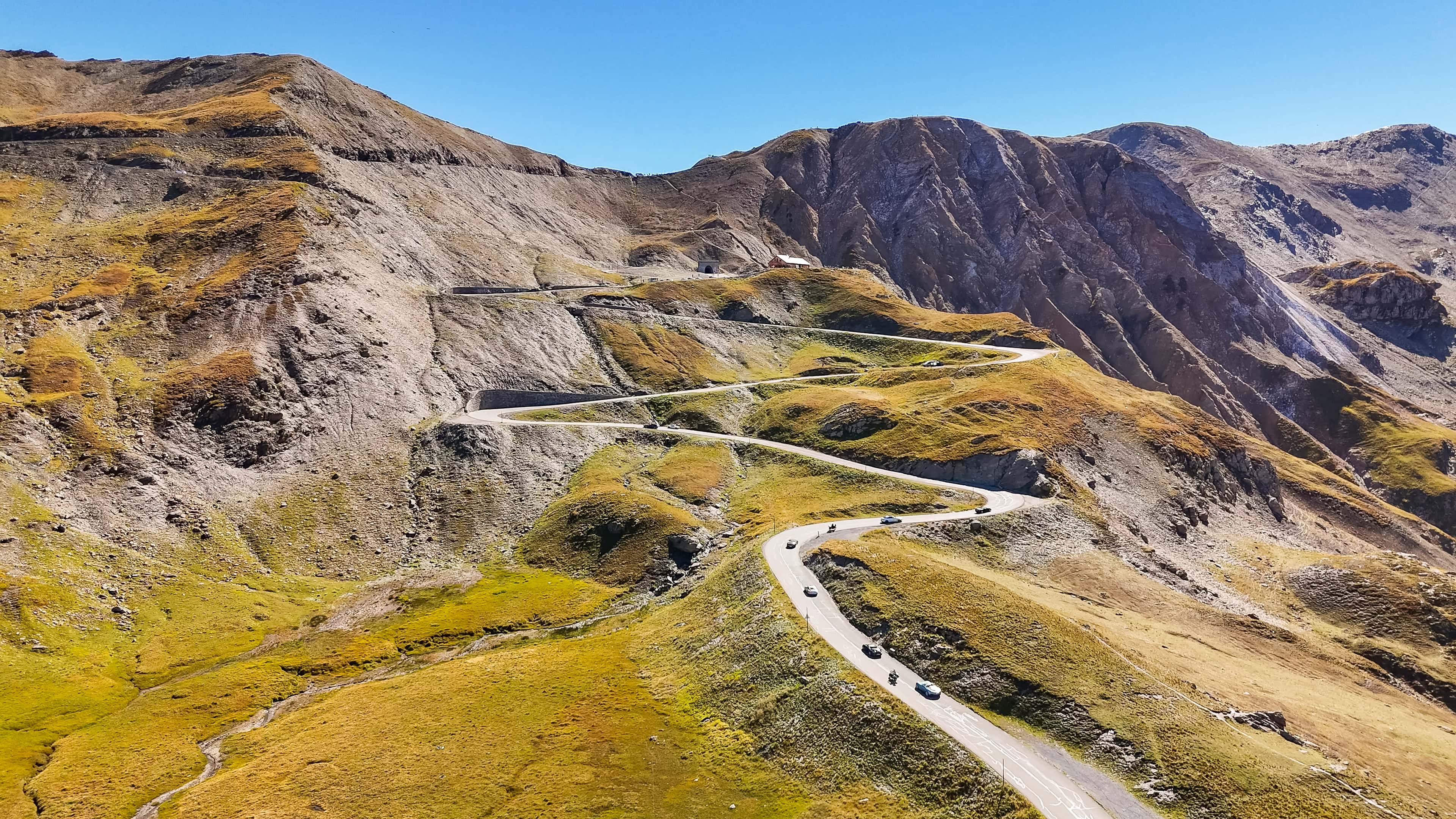 Gebirgspass mit Serpentinenstraßen und Autos in den Alpen bei strahlend blauem Himmel.