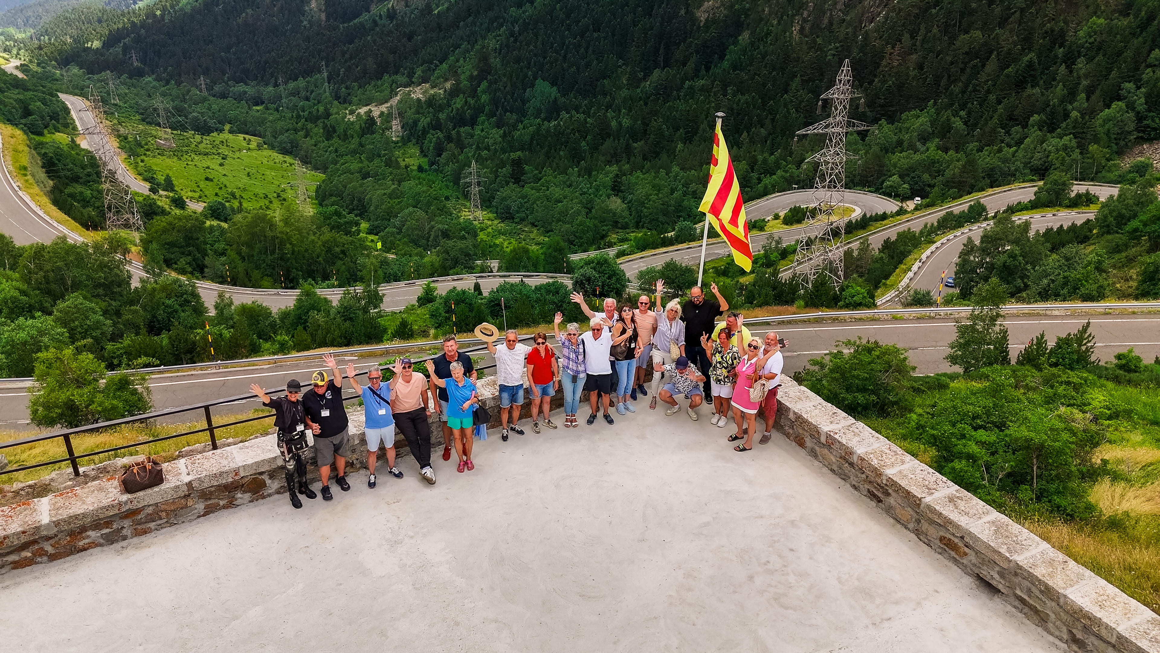 Gruppe von Reisenden vor einer malerischen Bergstraße in den Alpen.