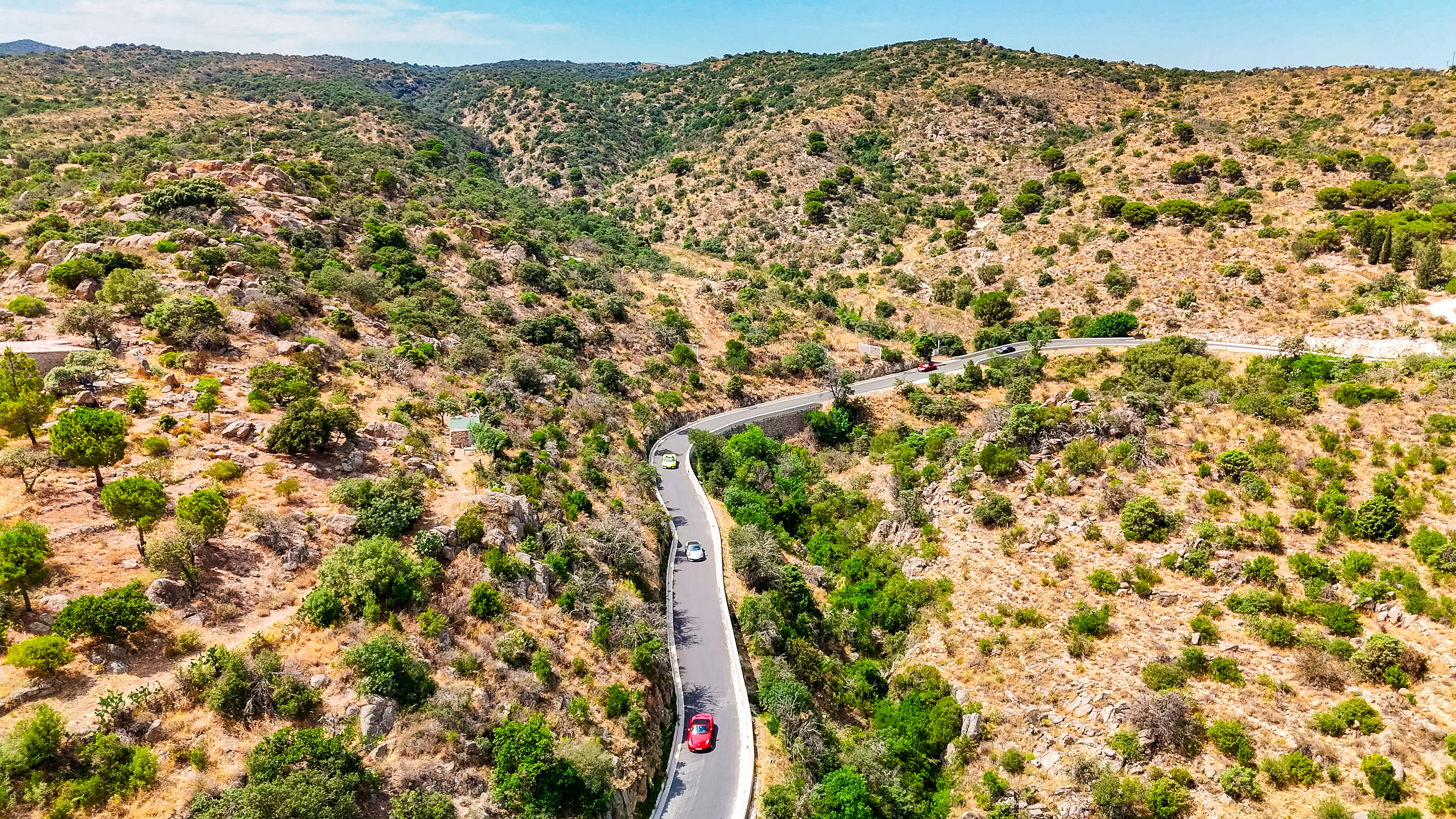 Sportwagen Erlebnisreisen: Drohnenaufnahme einer kurvenreichen Traumstraße durch die grüne Landschaft.