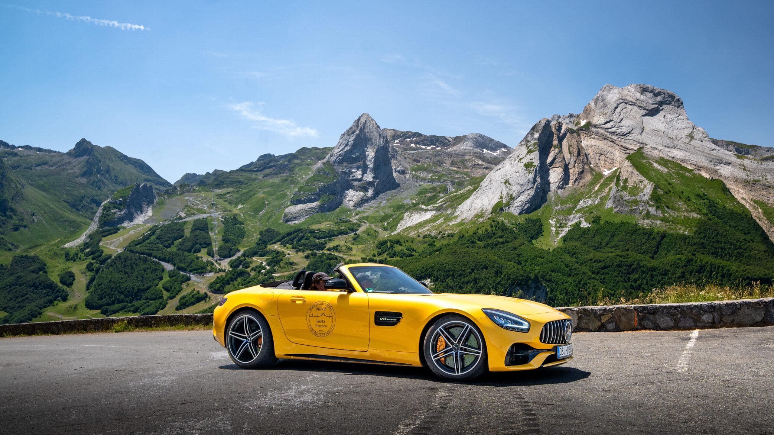 Ein leuchtend gelber Sportwagen vor majestätischen Berggipfeln in den Alpen, perfektes Reiseziel für Abenteuer.