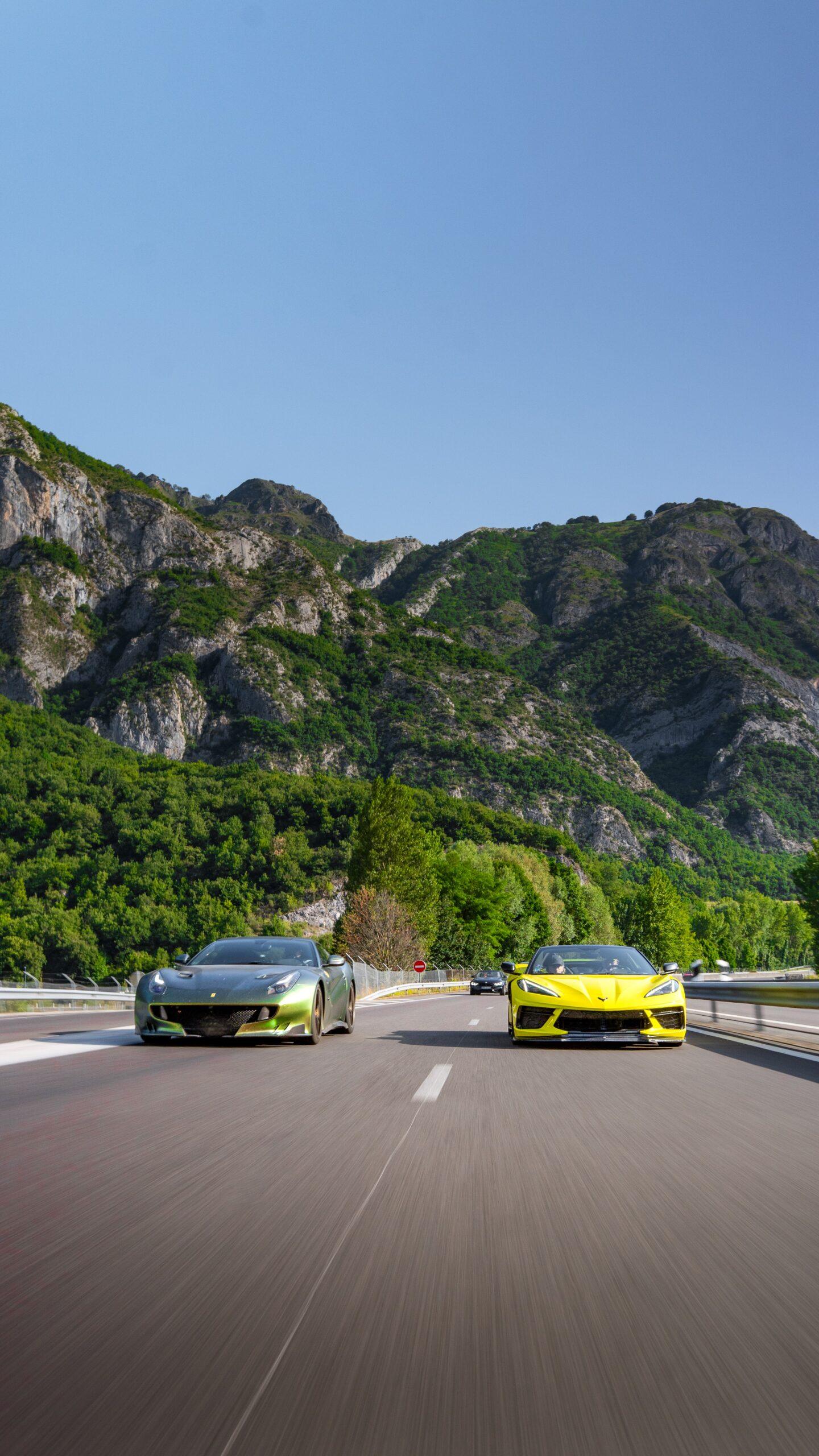 Sportwagen-Duo aus Ferrari und Corvette C8 auf gemeinsamer Fahrt durch eine majestätische Gebirgslandschaft.