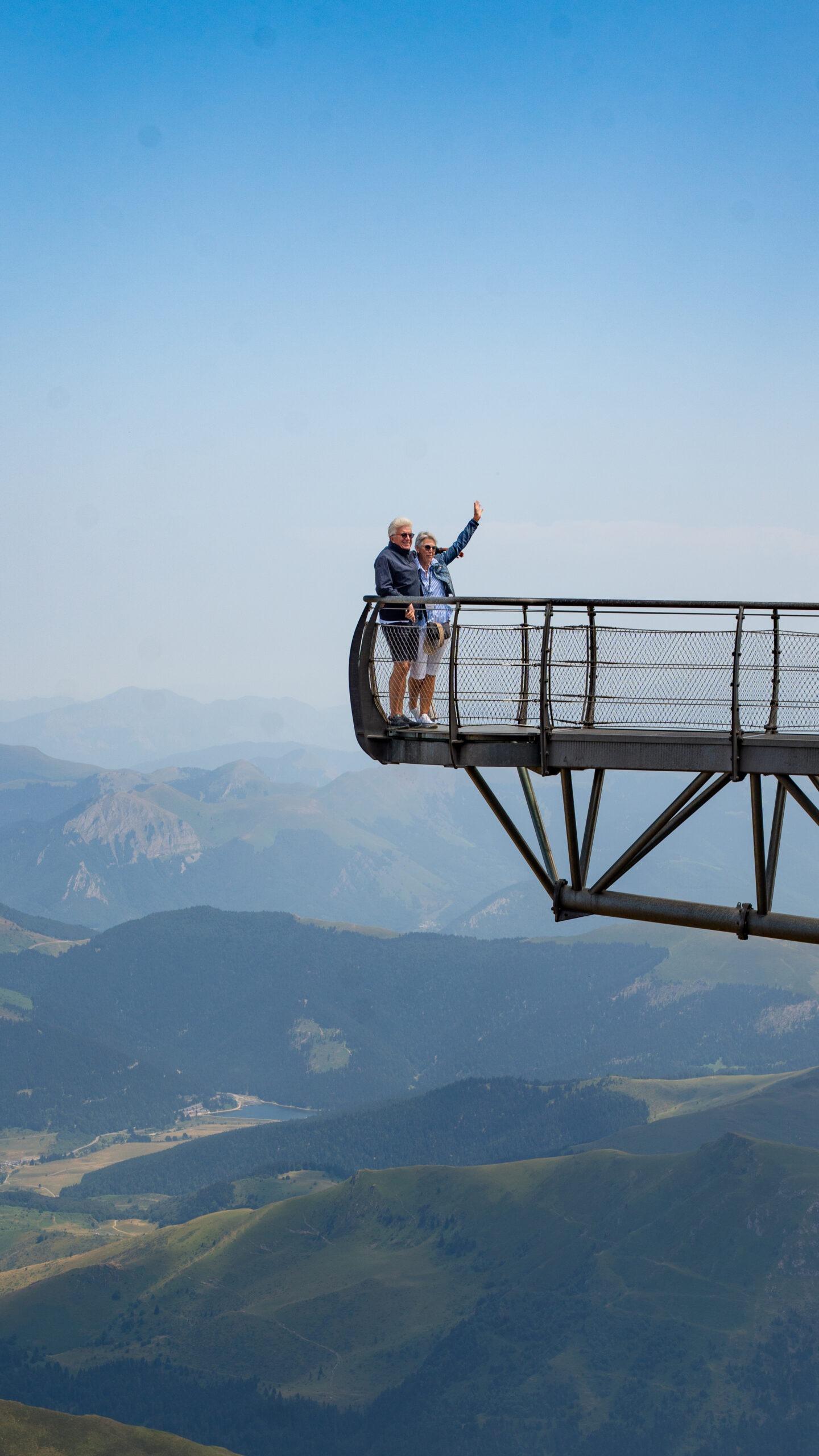 Winkende Reiseteilnehmer genießen den Ausblick von einer Plattform über den Bergen während der Tour.