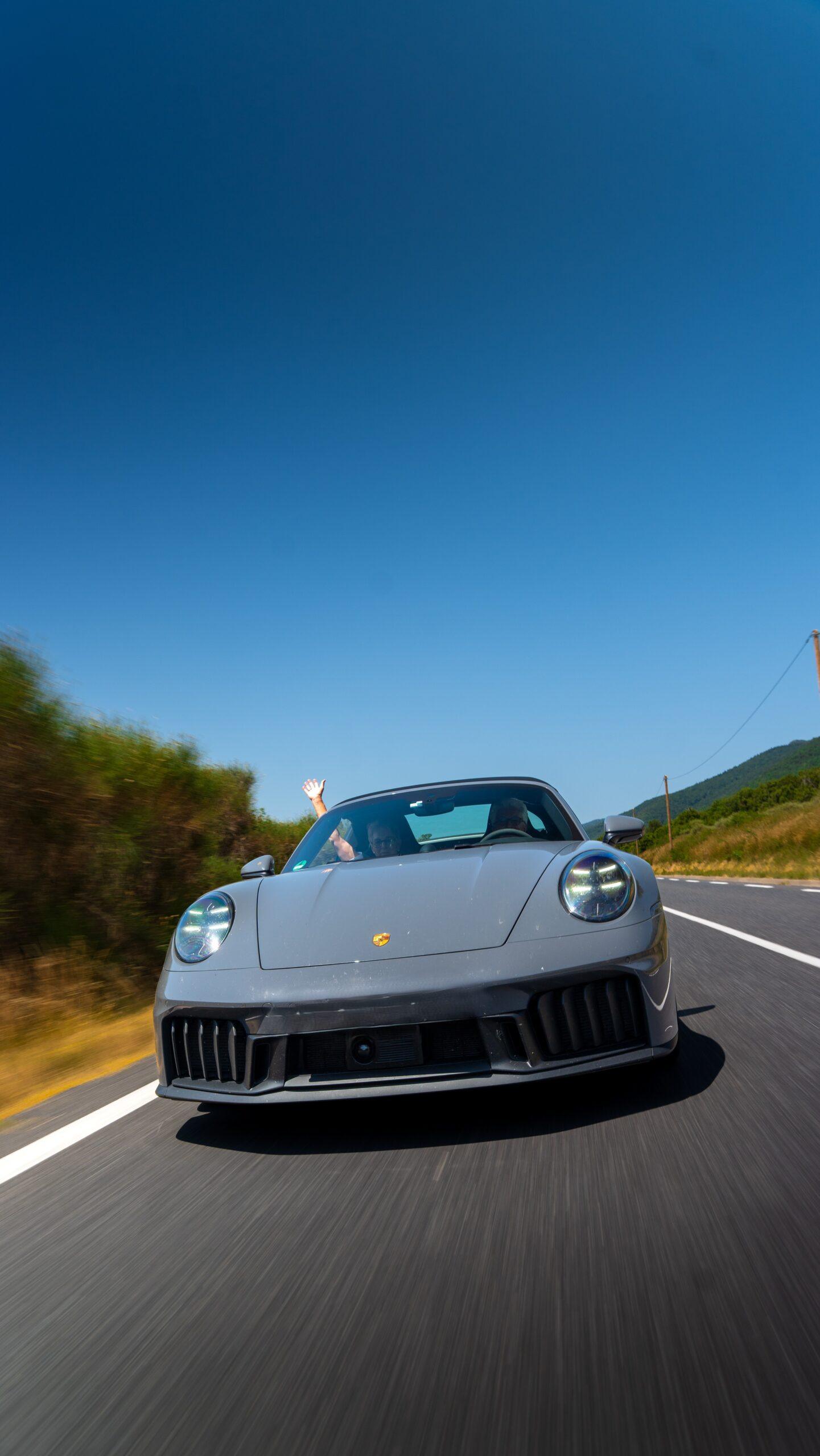 Grauer Sportwagen fährt auf malerischer Straße bei strahlendem Sonnenschein.