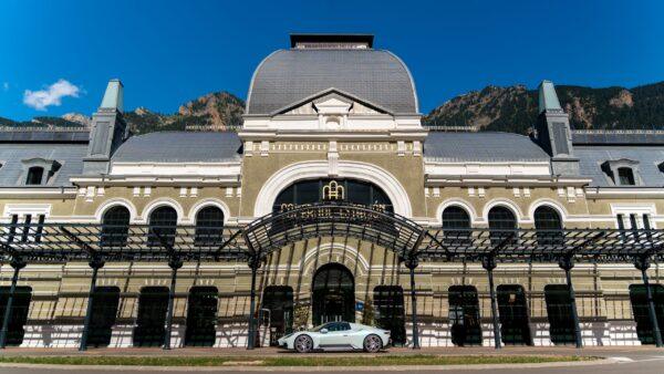 Eleganter Supersportwagen vor historischer Architektur in den Alpen unter strahlend blauem Himmel.