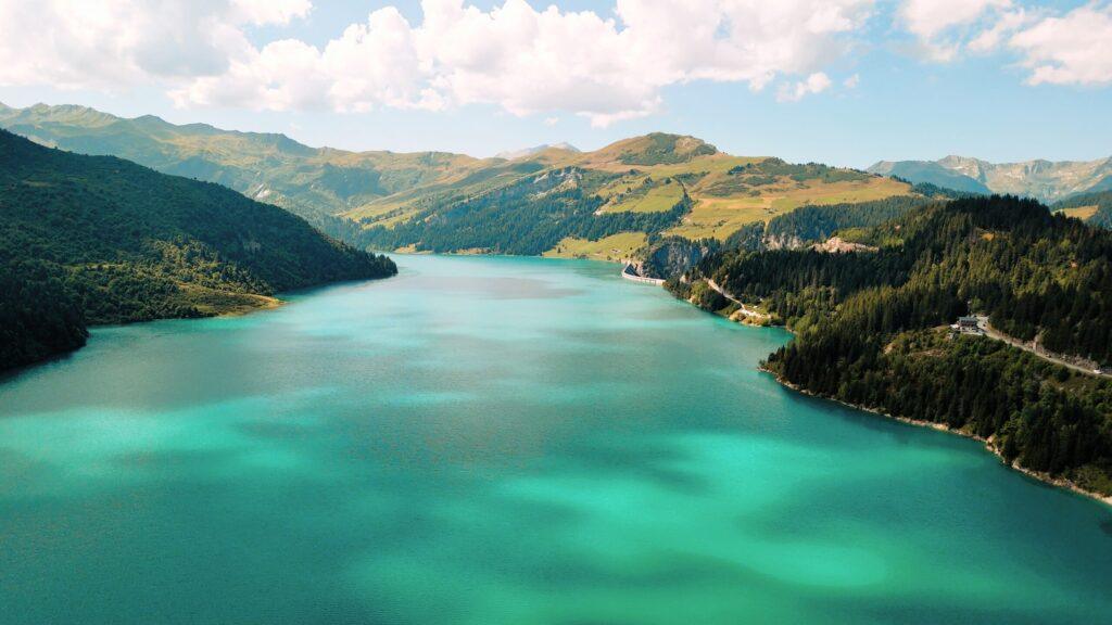 Kristallklarer See umgeben von majestätischen Bergen und üppiger Vegetation in den Alpen. Perfektes Ziel für Abenteuerreisen.