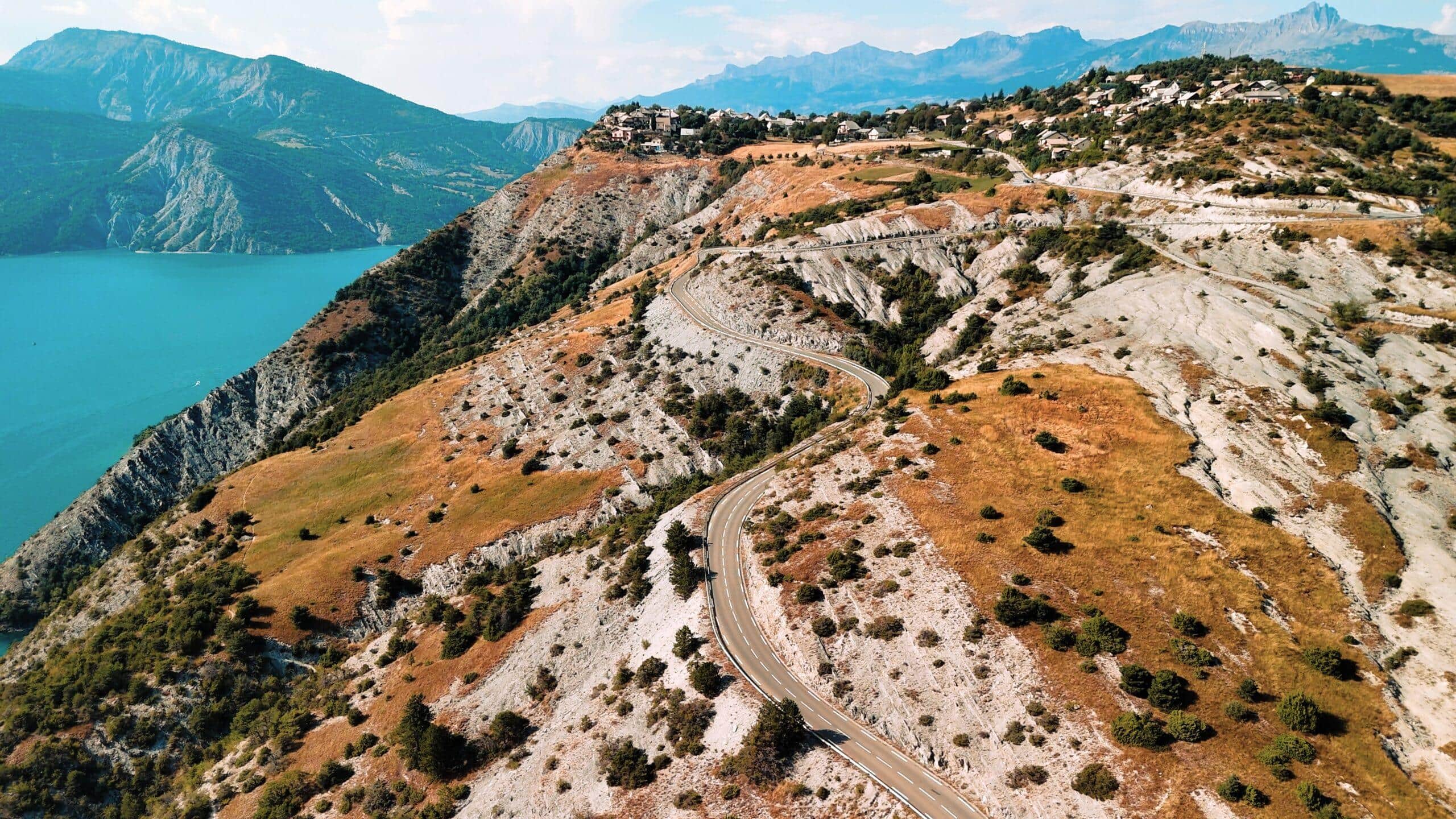 Kurvenreiche Straße entlang der Berghänge mit atemberaubendem Blick auf den türkisfarbenen See und die Alpenlandschaft.