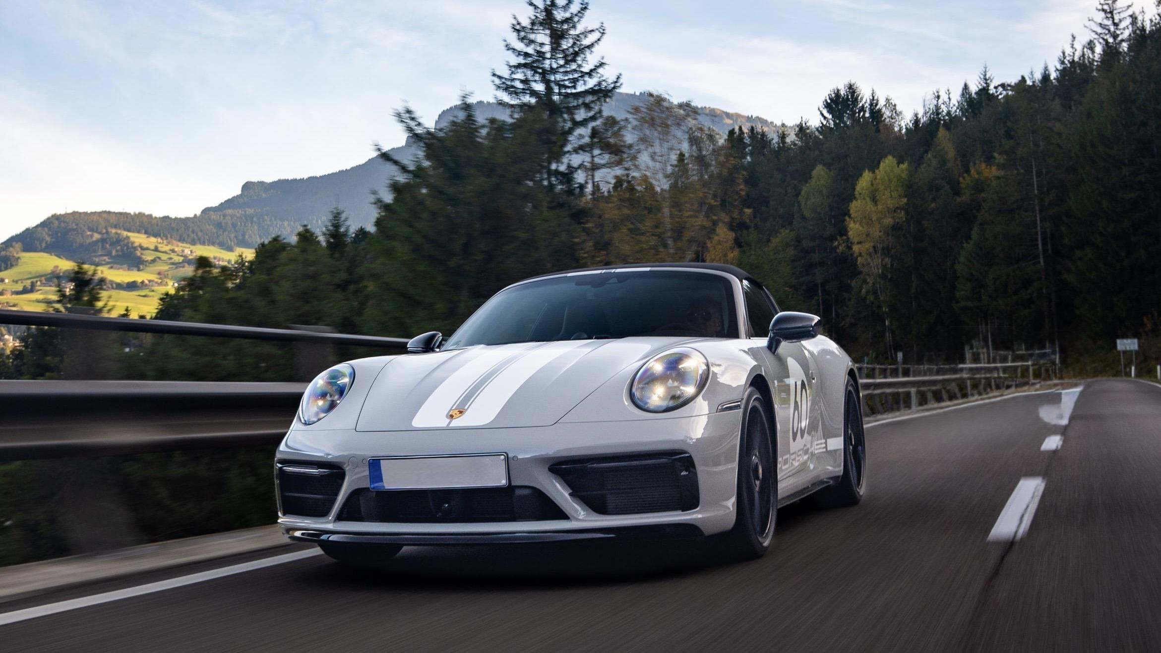 Silberner Sportwagen fährt durch malerische Alpenlandschaft auf einer kurvigen Straße.