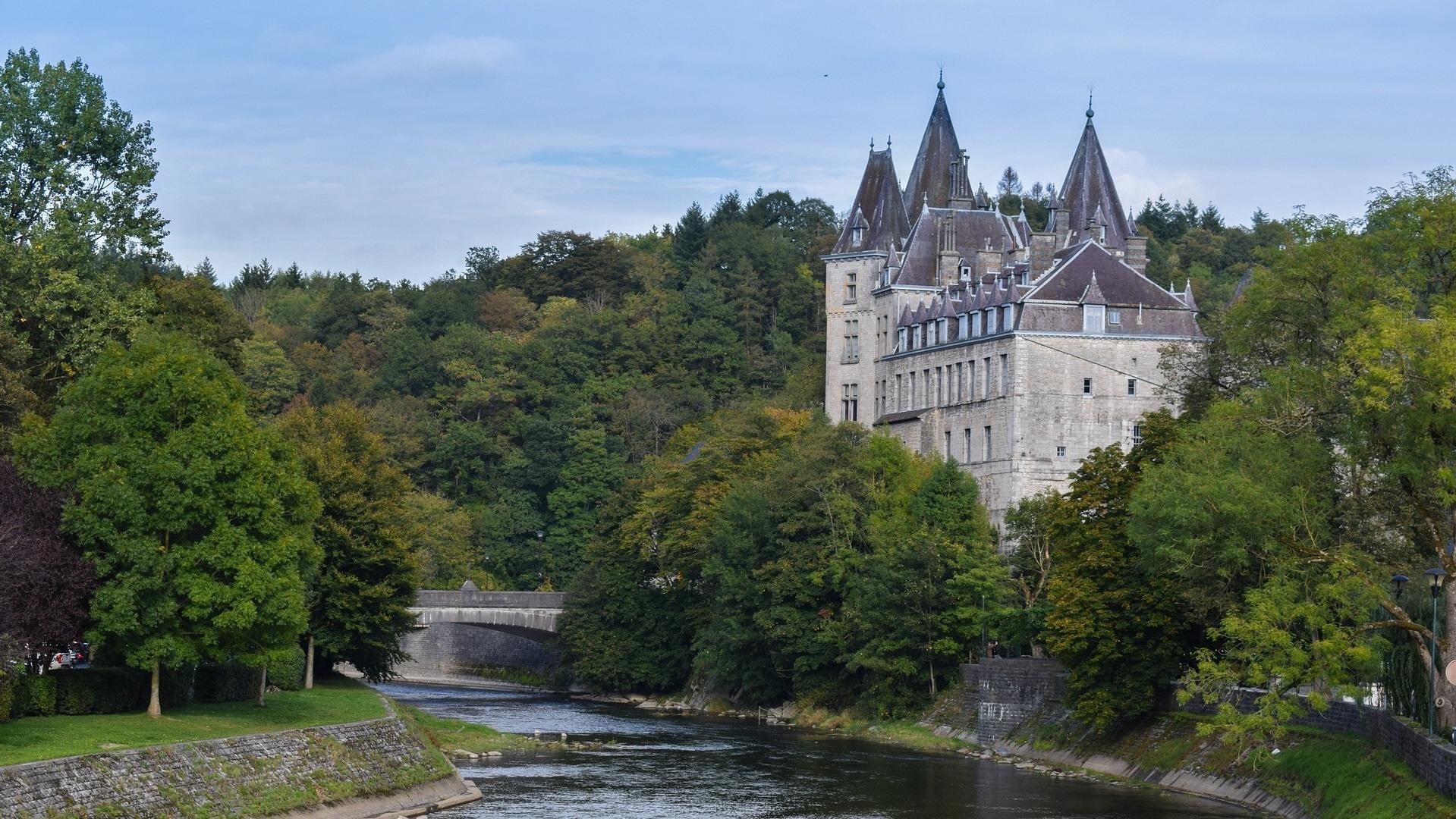 Ardennen Tour: Schloss Durbuy an einem Fluss, umgeben von dichtem Wald.