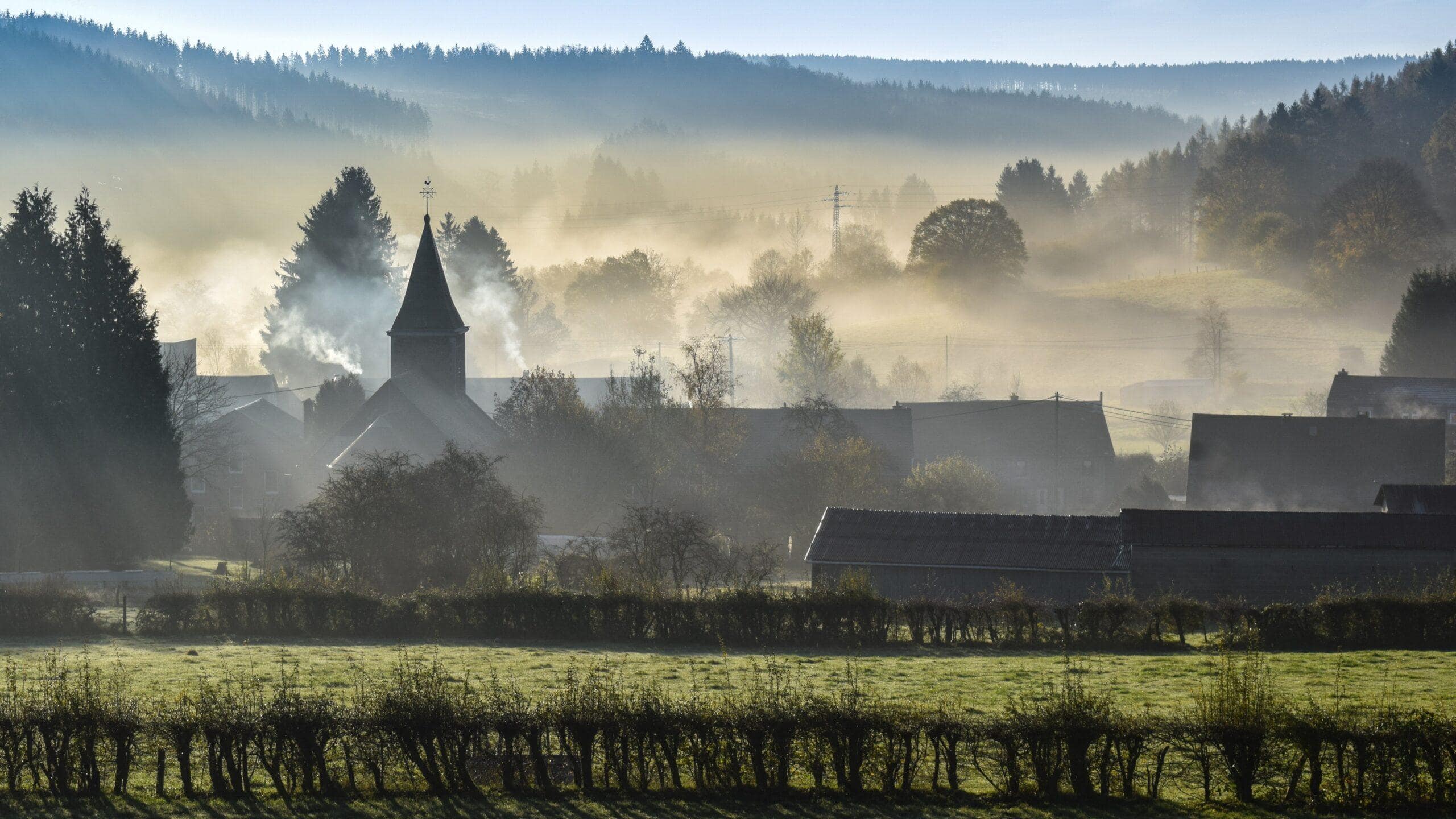Ardennen Tour: Morgennebel über einem kleinen Dorf mit Kirchturm in den Wäldern.